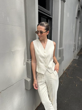 a lady in a beige worsted wool single-breasted vest with white pants